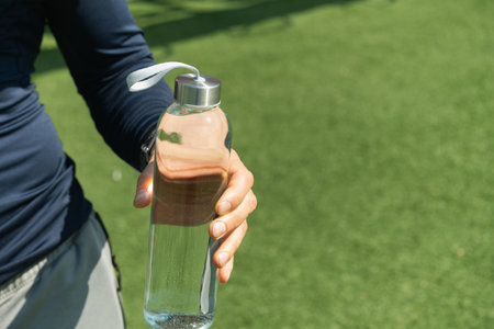 Water bottle in hand on outdoor sports ground. Concept water balance for heat season for workout....