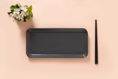 Empty rectangular gray plate for asian food with black chopsticks on pink background surface with...