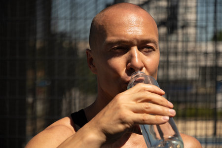 Athletes handsome man drinking water on outdoor sports ground. Water balance for active workout....