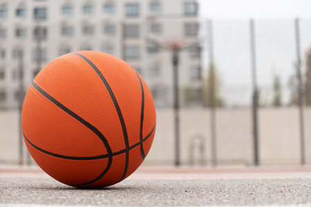 Outdoor public basketball court and basketball orange ball lies in front. Sports gear without people. Template, sport background. Copy space. Close up.