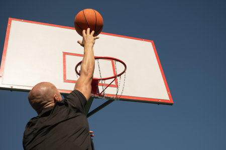 Basketball player or sporty man tries to throw ball into basketball hoop on sports court at...