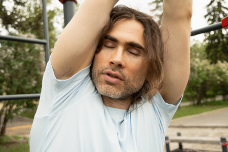 Man is tired of doing exercises. Hanging on horizontal bar at sports ground. Impact of bad weather. Close up.の写真素材