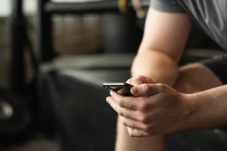 Young sporty man holding mobile phone while taking break in between exercises in gym. Close up.の写真素材