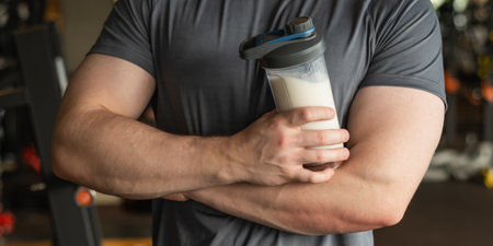 Sporty caucasian healthy fitness man with protein shake and cross hand. Athlete and professional trainer with sports nutrition beverage while working out. Health care and workout.の写真素材
