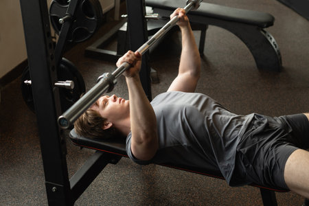Young caucasian man doing bench press exercise with barbell in fitness center or gym. Chest workout