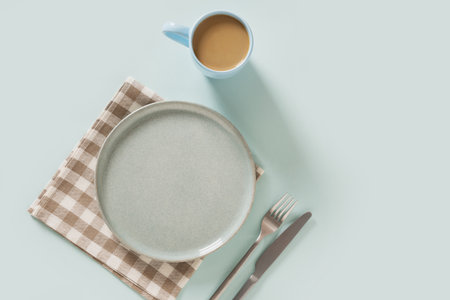 Empty ceramic blue plate, coffee and checkered napkin on plain light blue background. Table setting for breakfast. View from above. Copy spaceの写真素材