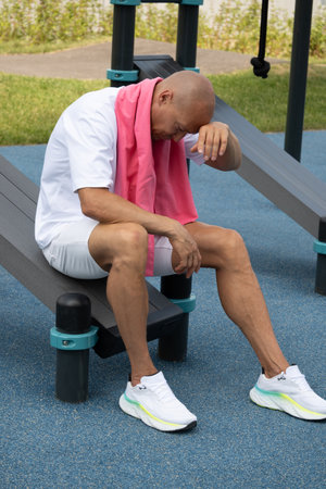 Sweaty athlete and sports man tired and sitting on bench with pink towel at urban sport ground after workout. Outdoor air training.の写真素材