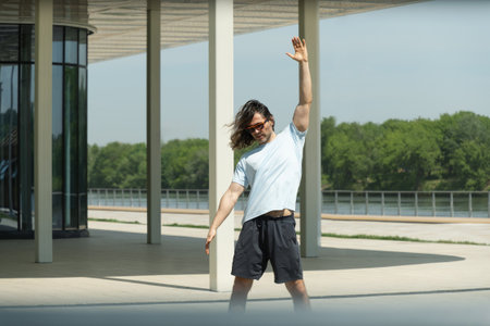 Fit brunette man wearing sports casual clothes doing stretching and warm up for arms on urban outdoor public park. Summer activity. Healthy lifestyle.の写真素材