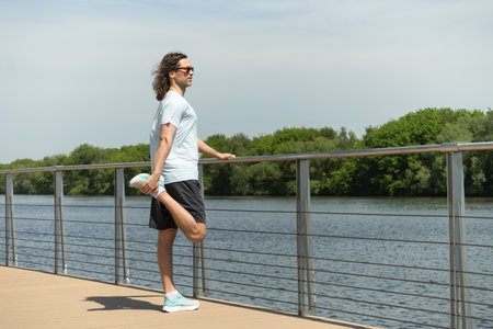 Fit handsome brunette man wearing sports casual clothes doing stretching legs exercise on city...