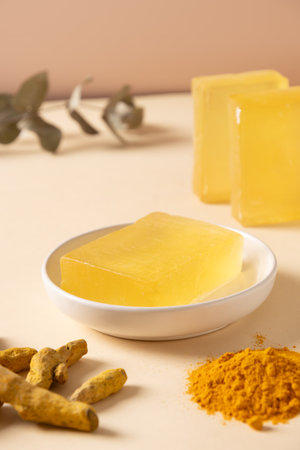 Handmade turmeric soap bar in white plate and curcuma root on beige background. Organic skincare product perfect for wellness, beauty, and organic body care concepts. Vertical. Close up.の写真素材