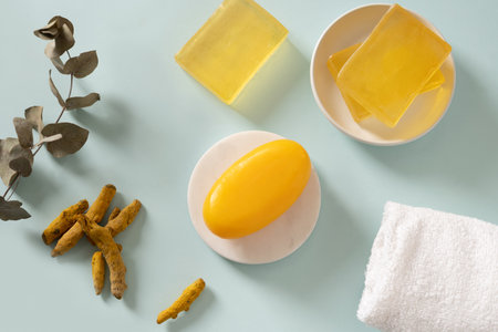 Handmade turmeric soap bar, powder and turmeric root on blue background. Organic skincare product perfect for wellness, beauty, and organic body care concept. View from above.の写真素材