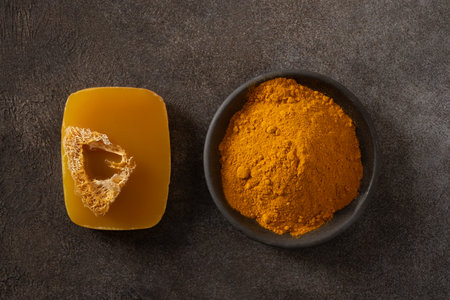 Turmeric soap bar and powder turmeric root on dark brown background. Organic skincare product perfect for wellness, beauty, and organic body care concepts. View from above.の写真素材