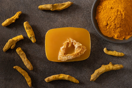 Turmeric soap bar and powder turmeric root on dark brown background. Organic skincare product perfect for wellness, beauty, and organic body care concepts. View from above.の写真素材