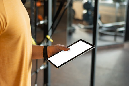 Personal trainer or bodybuilder holding tablet or clipboard in gym or fitness center with white...