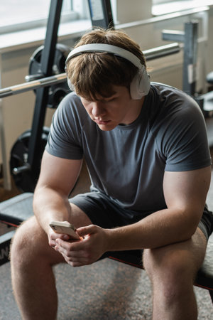 Young caucasian sporty man relax and sitting with mobile phone, listen music headphones and texting...
