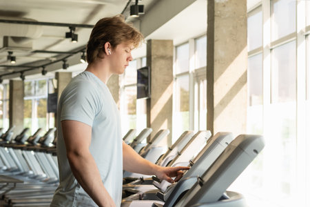 Athlete man wearing t-shirt running track, warming up on treadmill at gym. Close up.の写真素材