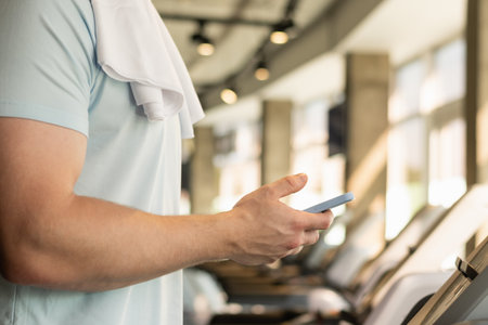 Sporty caucasian man with mobile phone checking apps and fitness progress on running track. Young...