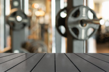 Wooden table surface in foreground with blurred gym background featuring weightlifting equipment. Fitness and healthy lifestyle themes. Space for design.の写真素材