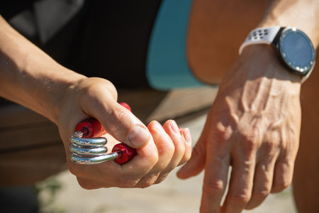 Man strengthens his grip using hand red metal expander. He is seen holding expander with firm grip,...