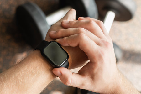Hand gym with smartwatch on wrist, set against background with gym equipment. Check fitness progress...