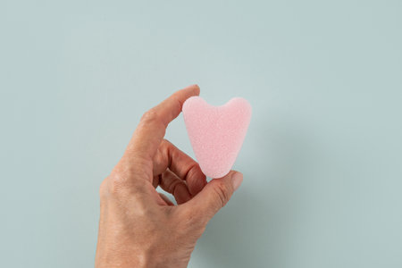 Pink stringless tampon as heart in woman hand on blue background. Hygiene accessories for women. View from above.の写真素材
