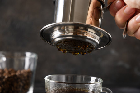 Brew Vietnamese coffee with sweet condensed milk in glass cup by traditional method on black...