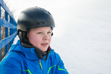 Young snowboarder caucasian boy in black helmet and blue jacket, standing outdoors on a snowy day. This is excited before winter sports adventure.の写真素材