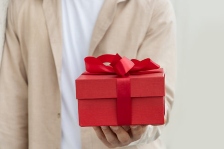 Red gift box with bow-knot in mans hand. Present with love for Birthday or Valentines Day. Greeting card. Close upの写真素材
