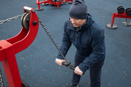 Adult male training on outdoor chain machine for triceps, wearing sportswear and hoodie, focused...