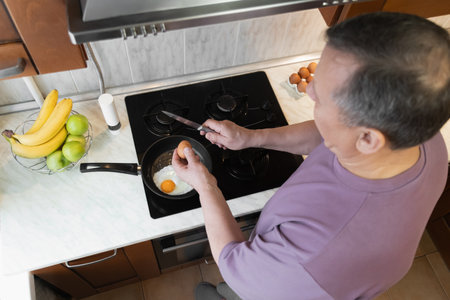 Man cooking fried eggs on a stovetop in a home kitchen, preparing a healthy morning meal with fresh ingredients. Morning Home Cooking Making and Eating Breakfastの写真素材
