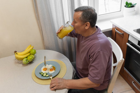 Man drinking fresh juice while having a healthy breakfast at home. Morning routine with nutritious food. Morning Home Cooking Making and Eating Breakfastの写真素材