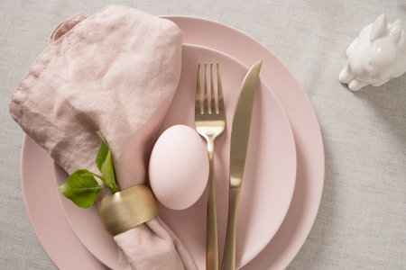 Easter table setting with pastel pink egg, gold cutlery and linen napkin on soft pink plate. Elegant spring decor.の写真素材