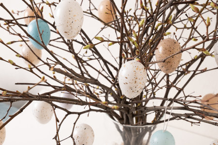 Spring Easter decor with natural branches and hanging pastel eggs arranged in glass vase. Spring...