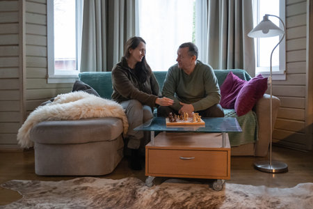 Mature couple sitting on sofa at home and spending time together playing chess, talking and relaxing...
