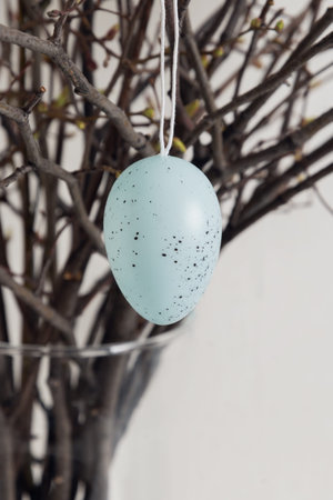 Close up detail of pastel Easter egg hanging on decorative branches creating minimal seasonal spring...