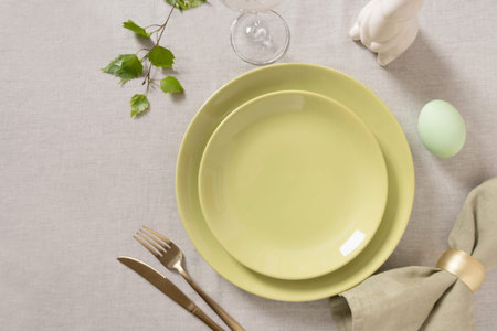 Empty pastel green Easter plate with gold fork, knife and linen napkin on light textile background....