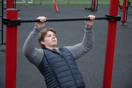 Young Man Performing Pull-Up Exercise at Outdoor Gym. Training Outdoors