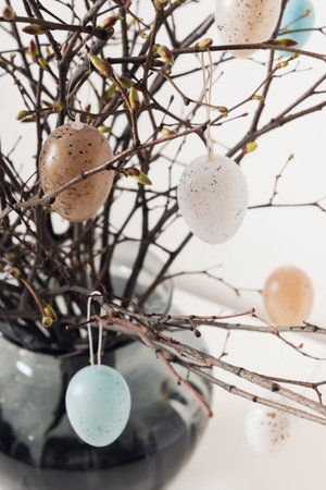 Easter tree decorated white and beige eggs in vase on white table. Close up.