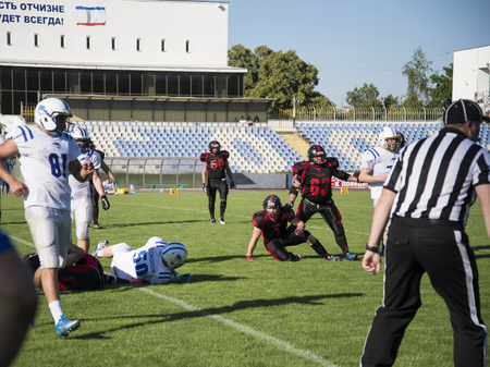Playing American football at the stadium. Teams for American football against the backdrop of a green field. Match on American football. Men play the ball in a sports stadium.のeditorial素材