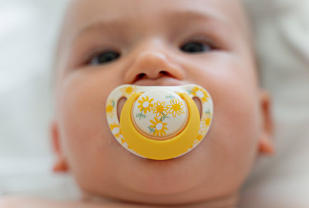 Baby in a diaper is lying on his back in a white blanket, sucking a pacifier. newbornの写真素材