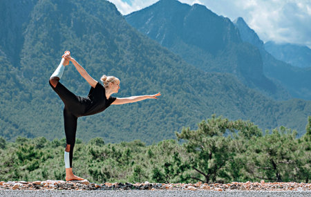 Woman doing yoga poses outside and beautiful view of mountains and sky with cloudsの写真素材