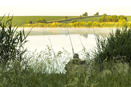 Summer sunny landscape. Morning, dawn on the lake. A fisherman sits on the shore with a fishing rod....