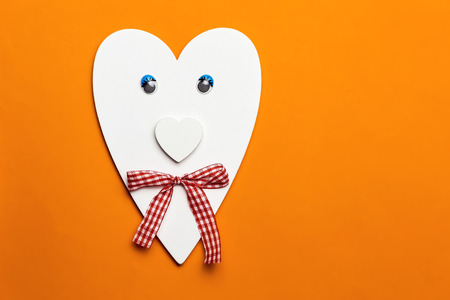 Children's orange background with creative wooden crafts, a symbol of love, a heart with eyes and a bow for mother's dayの写真素材