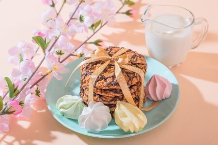 Fresh baked oatmeal crispy cookies on a blue plate on a background of peach color, milk, French...