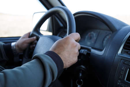 Man's hands hold steering wheel, driving a vehicle piloting a car in motion while traveling on a...