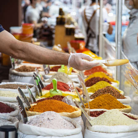 Sale of various natural fragrant Asian Indian spices in bags in an oriental bazaar, a man's hand in a glove offers sells goods in a scoop in a shop windowの写真素材