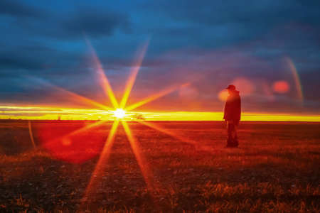 Man looks into the distance against the background of sunrise or sunset with sunbeams with a tree on...