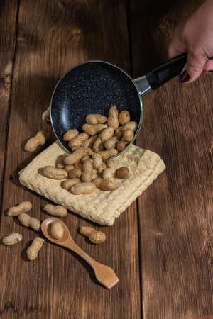 Leguminous plant is a source of vitamins, antioxidants, iron, hemoglobin and fiber, walnut contains niacin B3, roasted peanuts in shells in a pan on a table on a wooden backgroundの写真素材
