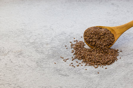 Flax seeds in a wooden spoon on a gray concrete background, a dietary product that reduces cholesterol, a natural source of omega-3, vitamins B and C, iodine, phosphorus, potassium, magnesium, nickelの写真素材