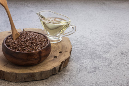 Linseed oil in a glass gravy boat and flaxseed in a wooden bowl vegetable source of omega-3, lowers cholesterol, used in food as a dietary salad dressing, in cosmetology, in herbal medicineの写真素材